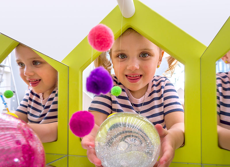 EduCasa Aufsatz Spiegelhaus mit bunten Pompoms und kleinem Mädchen mit glitzernder Kugel