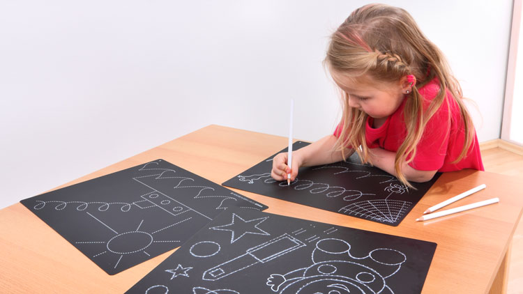 Ein Kind malt mit weissen Stiften auf schwarzem Papier