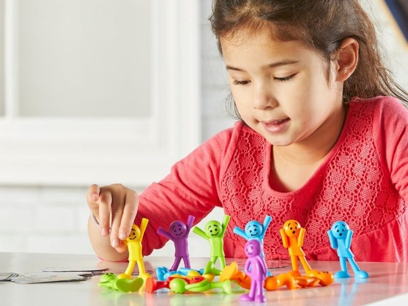 Mädchen sitzt am Tisch und spielt mit Figuren