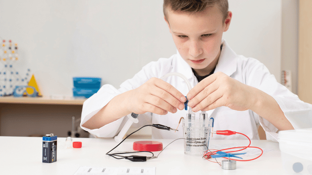 Junge mit Laborkittel sitzt am Tisch und experimentiert