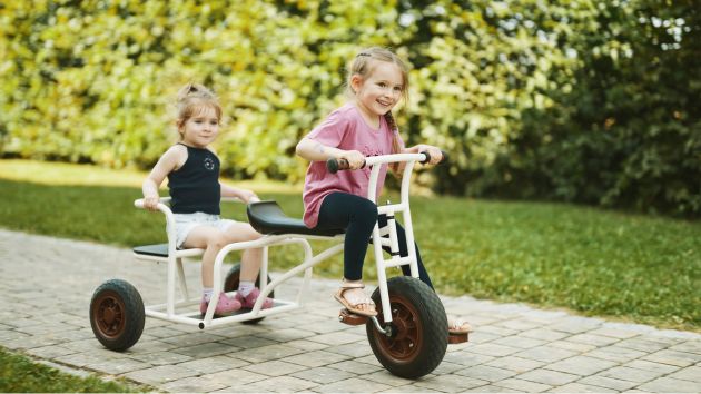 Zwei Kindergartenmädchen auf Kinderfahrzeug im Garten