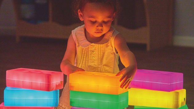 Experiment Leuchtbausteine Kleines Kind stapelt bunt leuchtende Bausteine in abgedunkeltem Raum