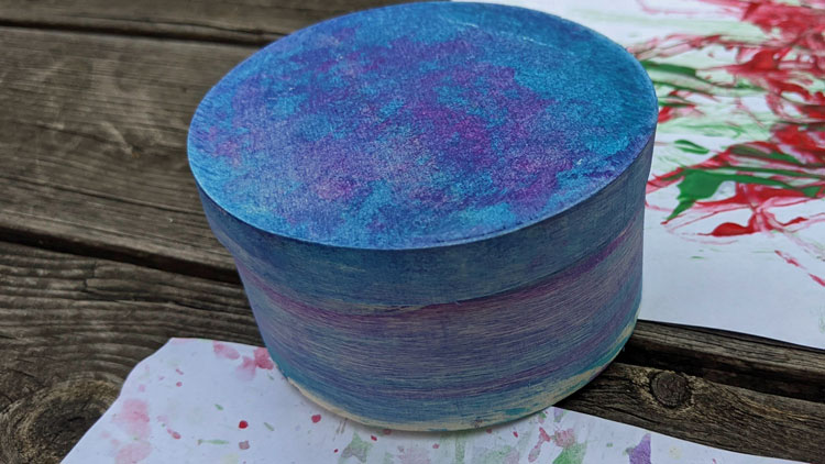 Holzbox mit einem Wollfaden und Fingerfarbe bemalt.