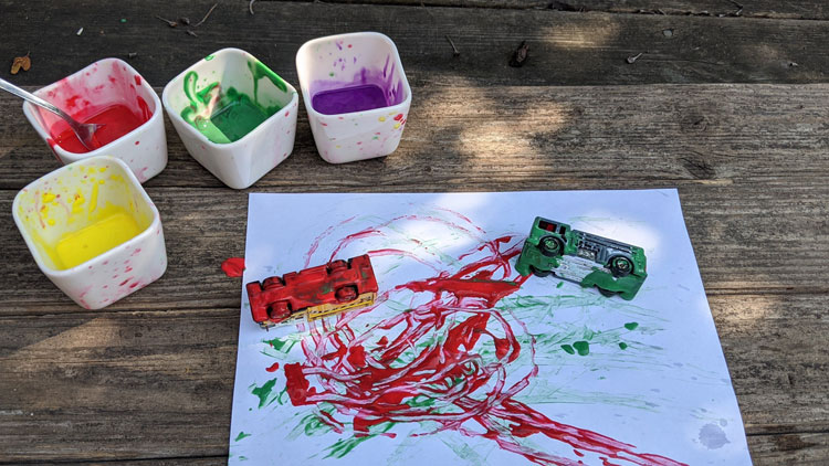 Mit Spielteugautos und Fingerfarbe entstehen bunte Bilder.