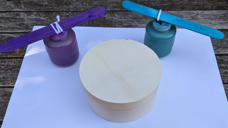 Wolle an ein Holzstäbchen geknotet wird in Fingerfarbe getaucht und als Malstift genutzt.