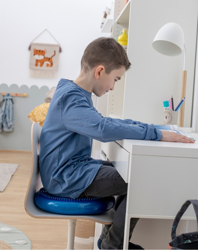 Sitzkissen Junge sitzt mit Sitzkissen auf einem Stuhl am Schreibtisch