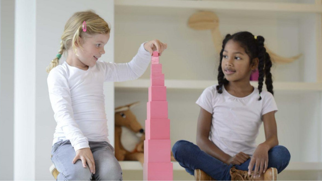 zwei Kinder sitzen am Boden und stapeln die Würfel des Rosa Turms