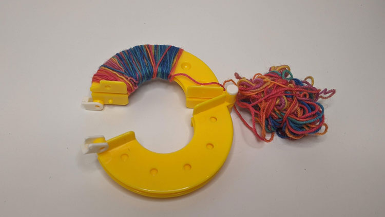 Pompon-Schablone mit Wolle aus dem Betzold Online-Shop umwickelt.