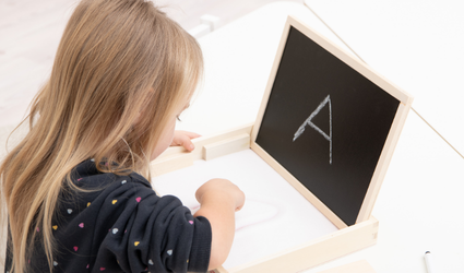 Mini-Sandwanne Mädchen zeichnet mit dem Finger den Buchstaben A in den Sand