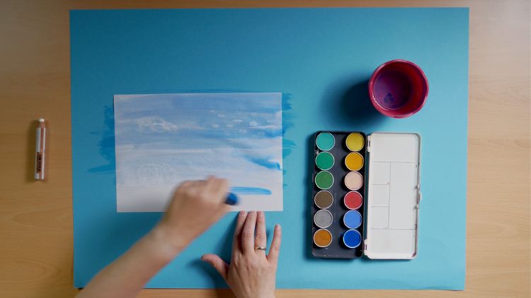 Mit weissem Wachsmaler und Wasserfarbe entstehen in Kindergarten und Kita farbenfrohe Wolkenbilder.