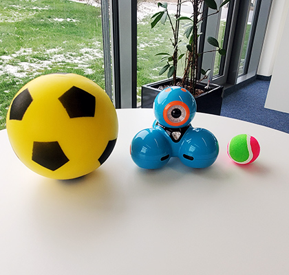 Dash-Roboter steht zwischen einem Fussball und einem Tennisball