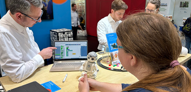 Zwei Personen unterhalten sich über Lernroboter, der vor ihnen auf dem Tisch steht